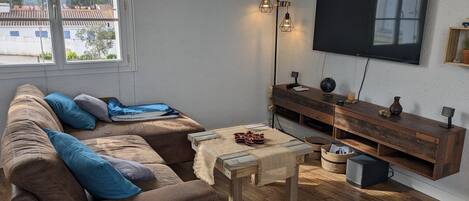 A living room with a brown sofa, a wooden coffee table, a TV mounted on the wall, and a wooden TV stand with a globe and a vase.