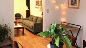 A living room with a sofa, a dining table, and a potted plant. - Miraflor Guest House, family and pet friendly (Sylva)