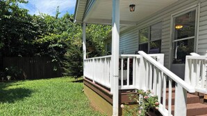 A house with a white porch, a small garden with a frog statue, and a wooden fence in the background. - Miraflor Guest House, family and pet friendly (Sylva)