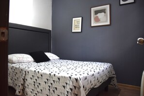 A bedroom with a bed, a headboard, a wall with two framed pictures, and a door. - The Fox Hostel (Santiago)