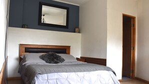 Quarto com uma cama, cabeceira de madeira, espelho na parede e uma porta.