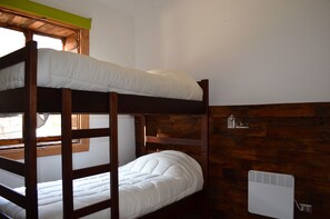 A bunk bed with a wooden frame and white bedding, a window with a wooden frame, and a white radiator on the wall. - The Fox Hostel (Santiago)