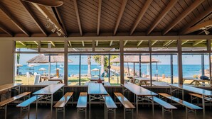 An outdoor dining area with wooden tables and benches, overlooking a beach with umbrellas and lounge chairs. - White s Landing Catalina Camp (Avalon)