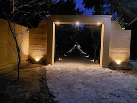 Uma passagem por um arco de pedra com luzes nas laterais, cercada por árvores.