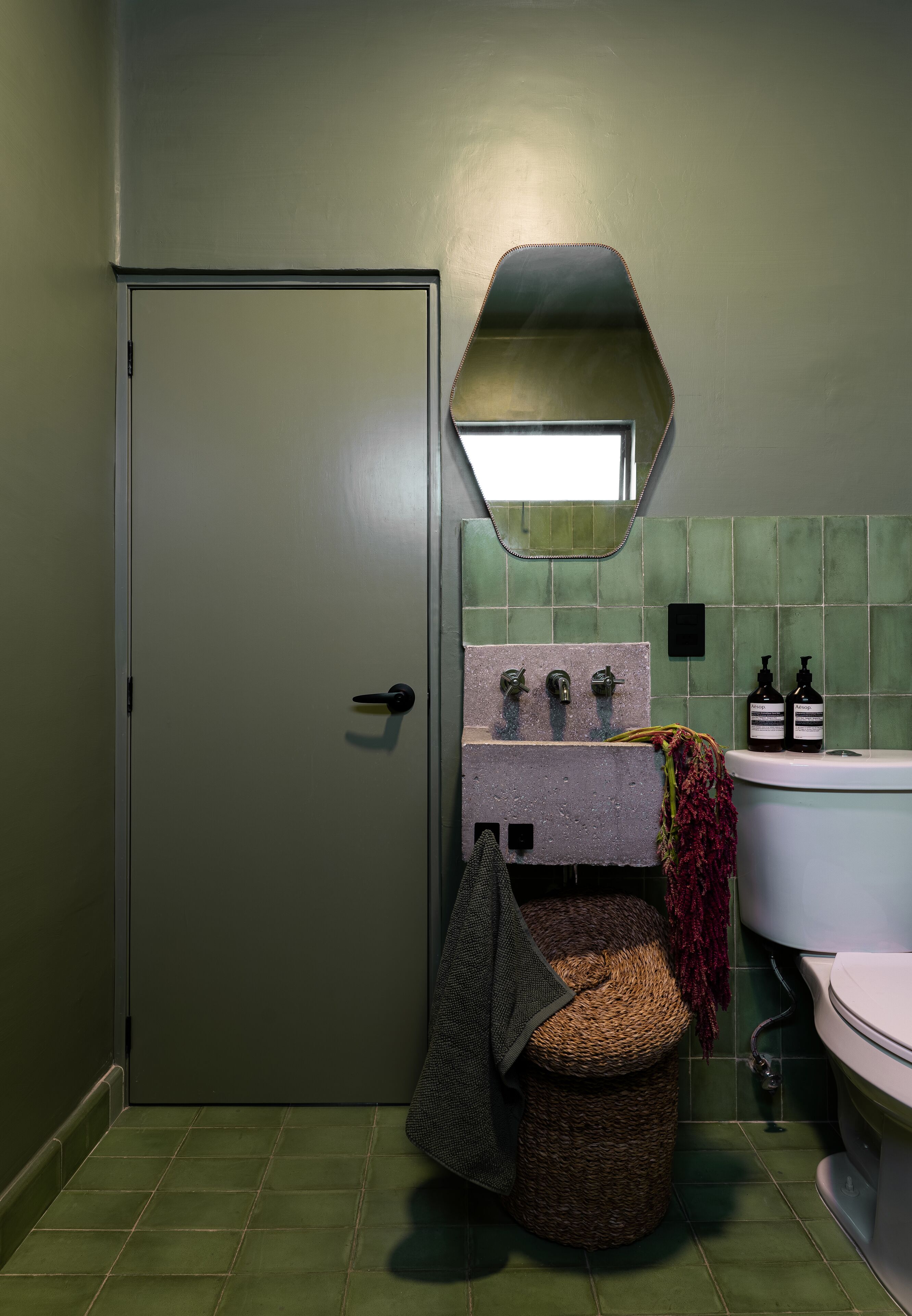 Un baño con puerta verde, un lavabo con espejo y un inodoro.