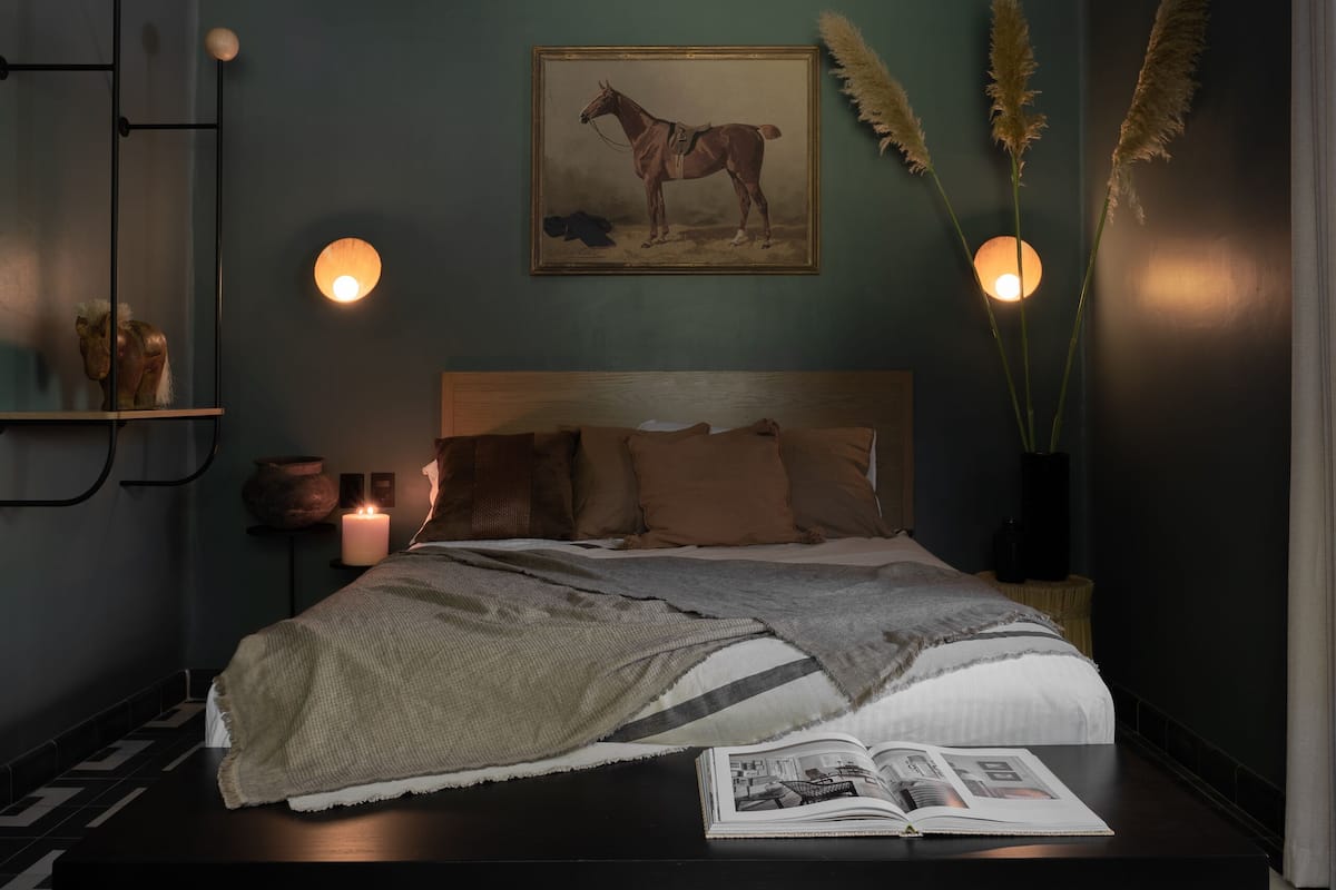 Une chambre à coucher comprenant un lit, des tables de chevet, une étagère fixée au mur, un tableau et une lampe sur pied.