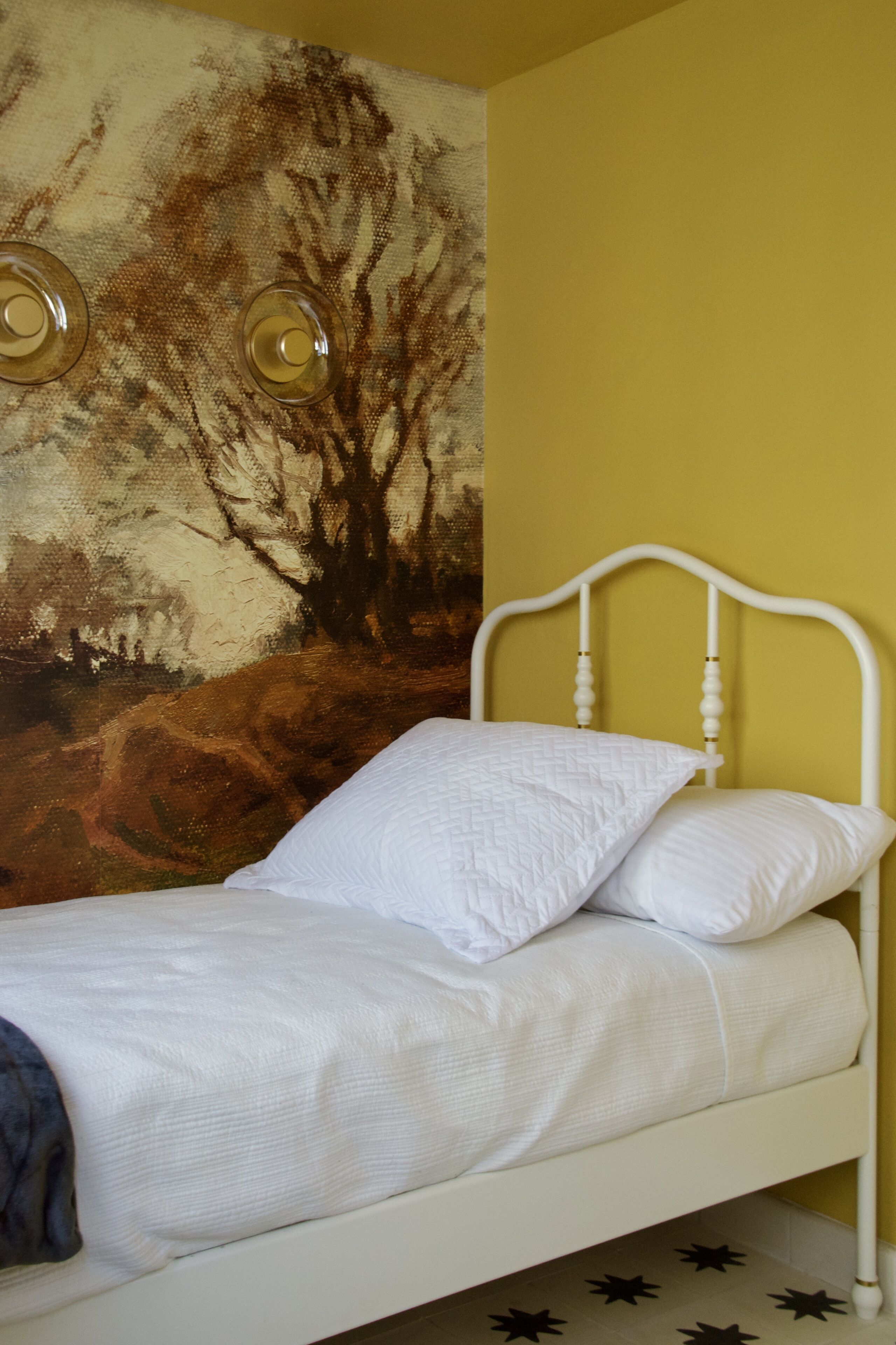 A bed with white bedding, a white headboard, and a wall with a landscape painting.