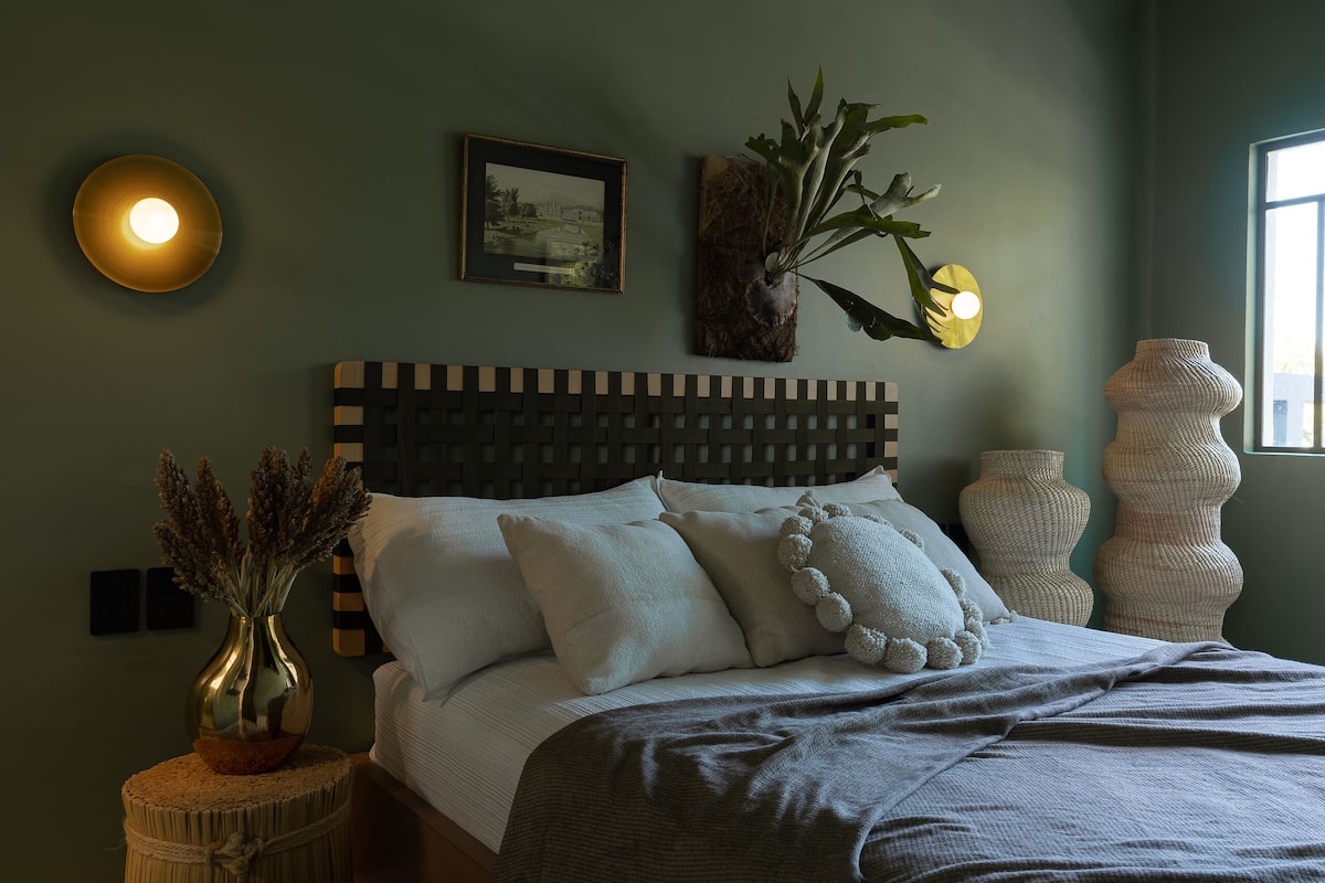 Une chambre à coucher avec un lit, des lampes de chevet, un tableau encadré et une fenêtre.