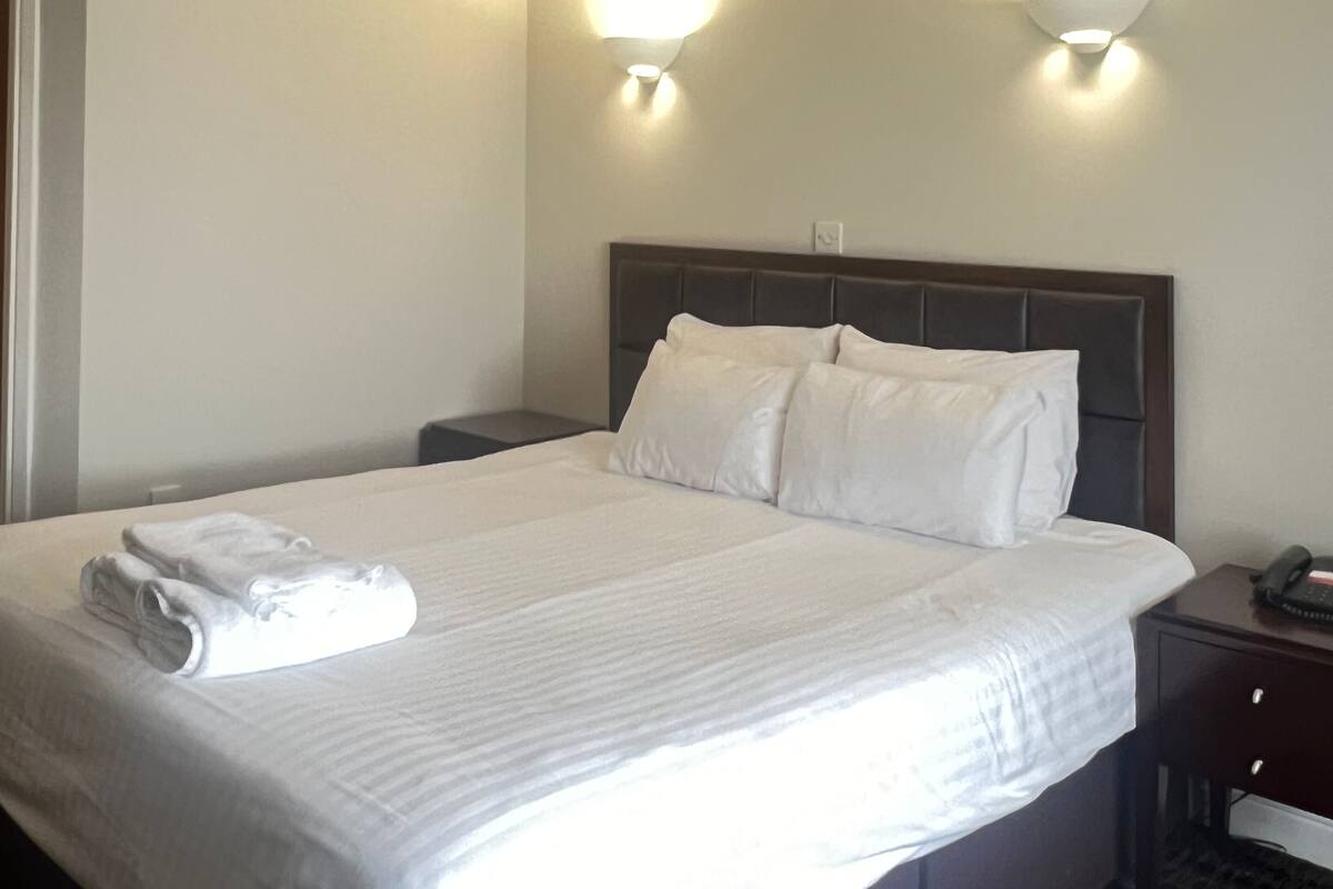 A hotel room with a large bed, two wall-mounted lights, a vent on the ceiling, and a bedside table with a phone.