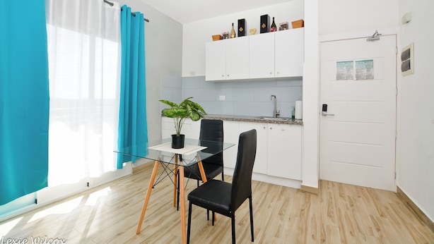 A modern kitchen with white cabinets, a black chair, a glass table, and a potted plant.