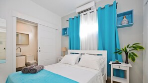 A bedroom with a bed, a nightstand, a potted plant, a shelf with a decorative item, and a bathroom visible through an open door. - One Suite & Beach 508 Top Floor Perfect 1BR Condo (Punta Cana)