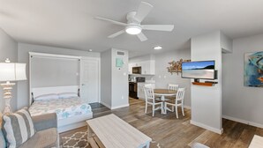 Ein modernes, helles Wohnzimmer mit einer Couch, einem Esstisch und einem Deckenventilator.