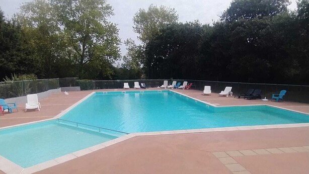 Una piscina rectangular amb terrassa enrajolada, envoltada per gandules i una tanca.