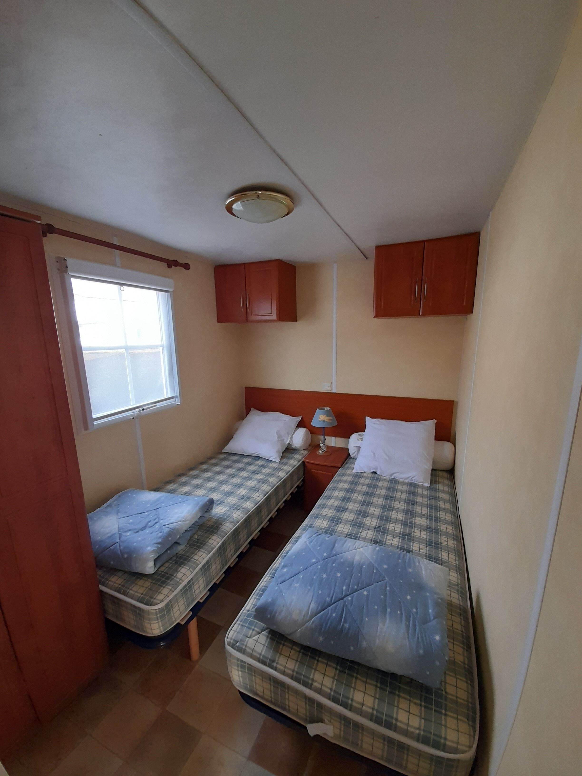 Quarto pequeno com duas camas, janela e armários de madeira.
