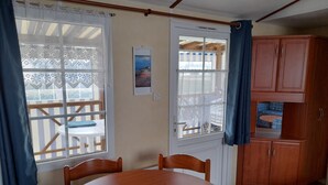 Una zona de menjador amb una taula rodona de fusta, cadires, una finestra amb cortines estampades i vista a l'exterior.