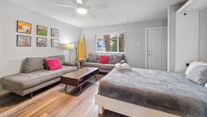 A modern bedroom with a bed, two sofas, a coffee table, and a ceiling fan. - Cozy Studio Large Pool w/ a Private Courtyard and a Block from the Beach (Port Aransas)