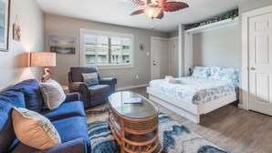A bedroom with a bed, a ceiling fan, a window, a nightstand, and a chair. - Cozy Studio Large Pool w/ a Private Courtyard and a 5 Min Walk to the Beach (Port Aransas)