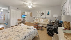 Amplia sala de estar con una cama grande, un sofá y una televisión. Se observan decoraciones de estrellas de mar en las paredes y un ventilador de techo.