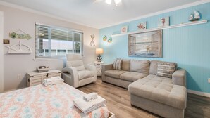 A bedroom with a bed, two sofas, a chair, a nightstand, and a ceiling fan. - Cozy Studio Large Pool w/ a Private Courtyard and a 5 Min Walk to the Beach (Port Aransas)