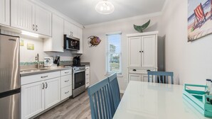 A modern kitchen with white cabinets, stainless steel appliances, and a teal dining table. - Cozy Studio Large Pool w/ a Private Courtyard and a 5 Min Walk to the Beach (Port Aransas)