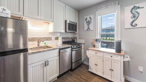 A modern kitchen with white cabinetry, stainless steel appliances, a granite countertop, and a window with blinds. - Cozy Studio Large Pool w/ a Private Courtyard and a 5 Min Walk to the Beach (Port Aransas)