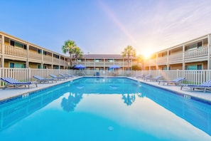 A swimming pool with lounge chairs and umbrellas, surrounded by a multi-story building with balconies. - Cozy Studio Large Pool w/ a Private Courtyard and a 5 Min Walk to the Beach (Port Aransas)