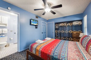 A bedroom with a bed, a ceiling fan, a television, and a bathroom visible through an open door. - Roomy 1 BDRM Large Pool w/ a Private Courtyard and a 5 Min Walk to the Beach (Port Aransas)