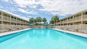 A swimming pool with lounge chairs and umbrellas, surrounded by a multi-story building with balconies.