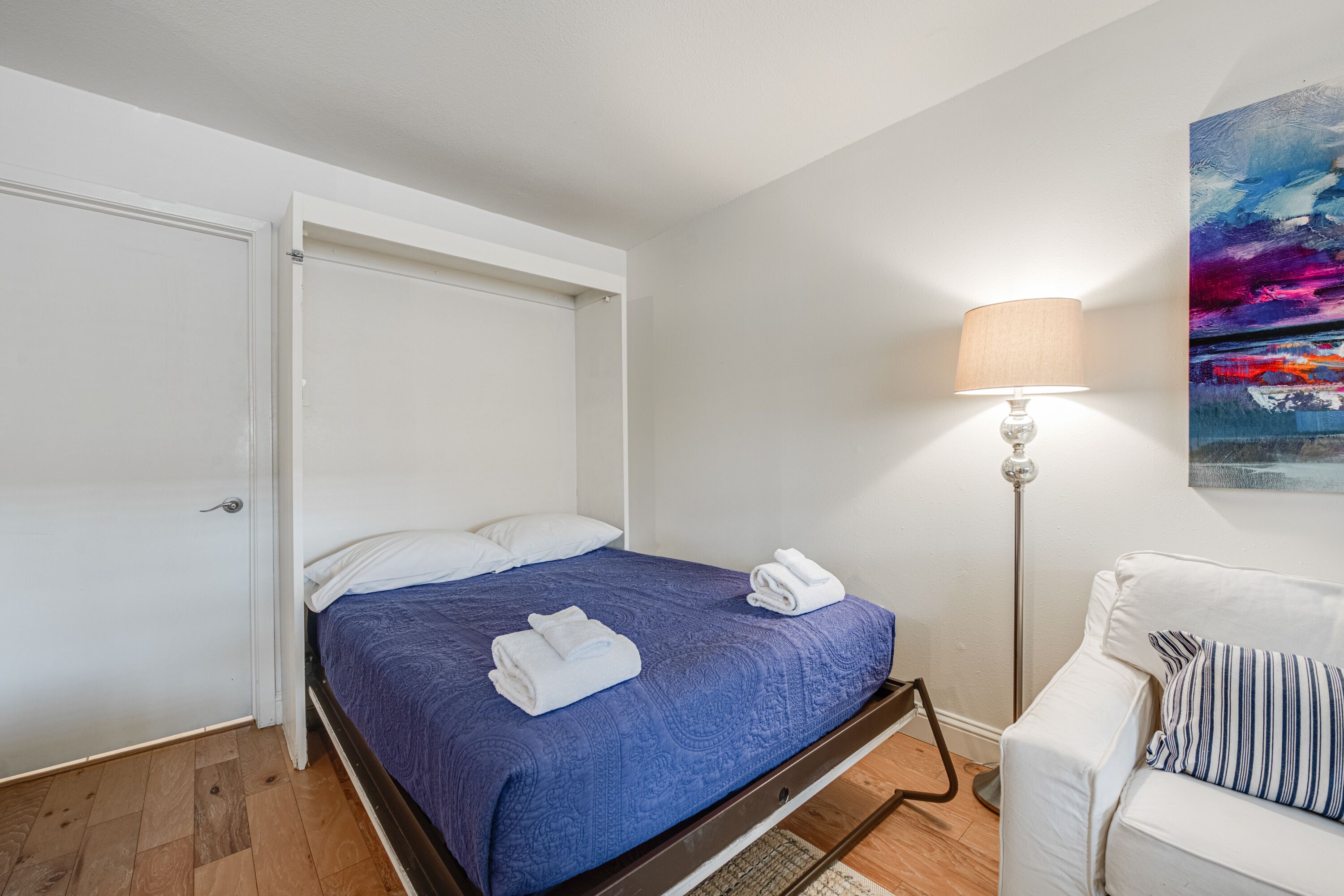 Ein Schlafzimmer mit einem Bett, einem weißen Sessel, einer Stehlampe und einem Bild an der Wand.