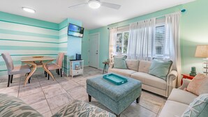 Un salon avec un mur à rayures turquoise, un canapé beige, une table à manger avec des chaises et un ventilateur de plafond.