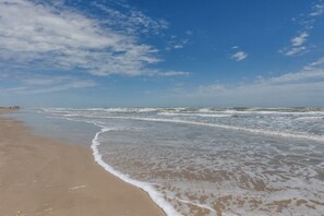 Ein Strand mit sanft anschwellenden Wellen unter blauem Himmel.