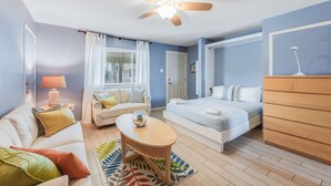 Une pièce bien éclairée, avec un ventilateur de plafond, un lit, un canapé, une petite table et une commode.