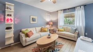 Un salon doté d’un ventilateur de plafond, de deux canapés, d’une table basse et d’une fenêtre avec des rideaux.