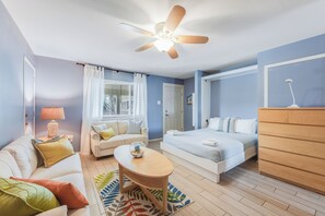 A well-lit room with a ceiling fan, a bed, a sofa, a small table, and a dresser. - Cozy Studio Large Pool w/ a Private Courtyard and a 5 Min Walk to the Beach (Port Aransas)