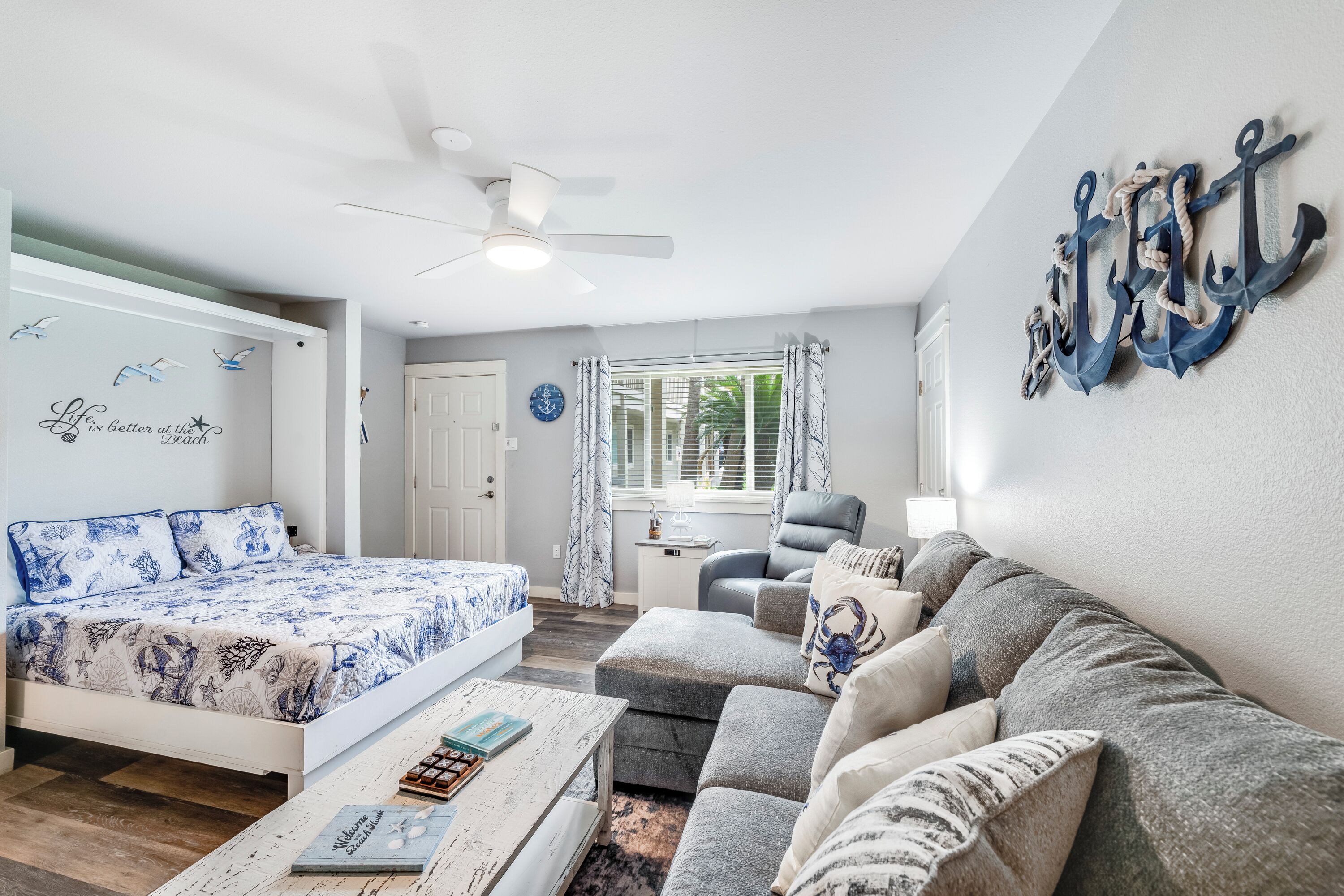 Ein Schlafzimmer mit einem Bett, einem Sofa, einem Couchtisch, einem Sessel, einem Deckenventilator und einem Fenster mit Vorhängen.