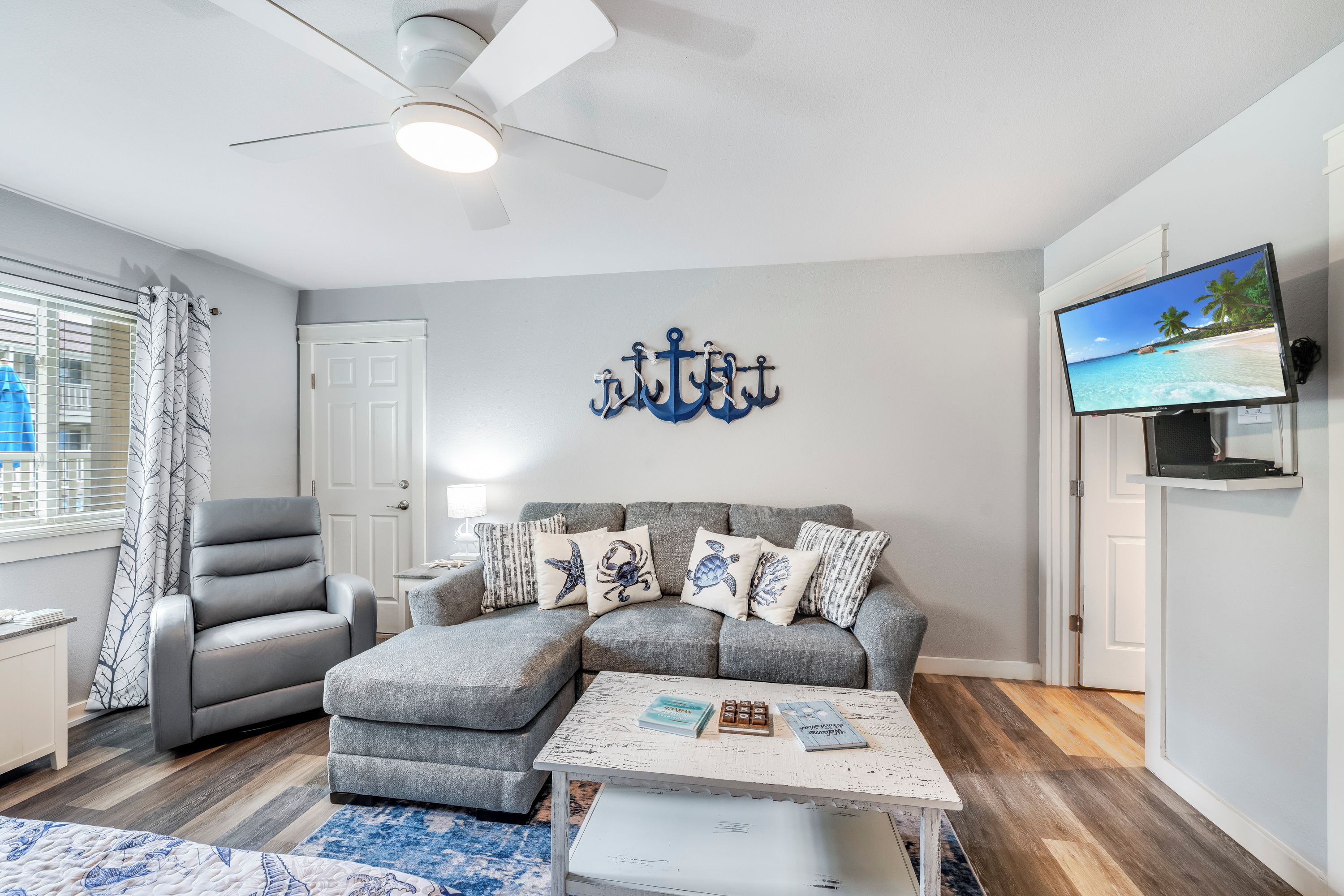 A living room with a grey sectional sofa, a white coffee table, and a wall-mounted TV.