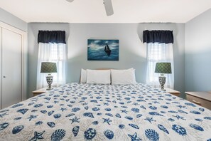 A bedroom with a bed, two nightstands, a window with curtains, a painting of a sailboat, and a patterned bedspread. - Roomy 1 BDRM Large Pool w/ a Private Courtyard and a 5 Min Walk to the Beach (Port Aransas)