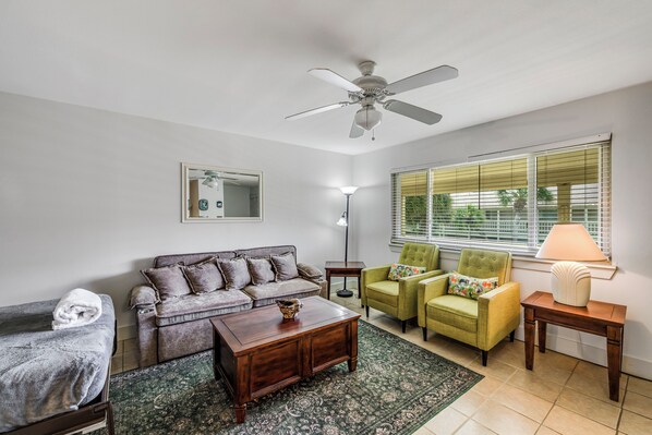 A living room with a ceiling fan, a sofa, two armchairs, a coffee table, a lamp, and a window with blinds.