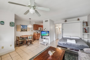 A modern hotel room with a bed, a TV, a dining area with a table and chairs, a kitchen area, and a ceiling fan. - Roomy 1 BDRM Large Pool w/ a Private Courtyard and a 5 Min Walk to the Beach (Port Aransas)