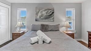 A bedroom with a large bed, two bedside tables with lamps, a window with blinds, and a painting of a wave on the wall. - Roomy 1 BDRM Large Pool w/ a Private Courtyard and a 5 Min Walk to the Beach (Port Aransas)
