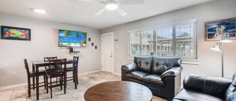 A living room with a dining area, a black leather sofa, a round coffee table, and a ceiling fan.