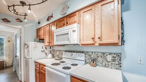 Una cocina con armarios de madera, un microondas blanco, una estufa y un refrigerador.