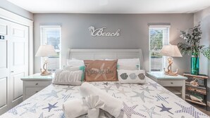 Ein Schlafzimmer mit einem Bett mit Sternfisch-Muster, einem Kissen mit dem Aufdruck 'Beach' und 'Senses the Day' sowie einem Wandschild mit der Aufschrift 'Beach'.