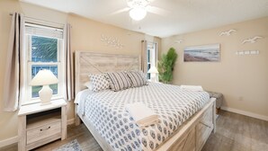 A bedroom with a bed, nightstand, lamp, window, ceiling fan, and wall art. - Roomy 1 BDRM Large Pool w/ a Private Courtyard and a 5 Min Walk to the Beach (Port Aransas)