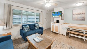 A living room with a sofa, a coffee table, a TV, and a painting on the wall. - Roomy 1 BDRM Large Pool w/ a Private Courtyard and a 5 Min Walk to the Beach (Port Aransas)