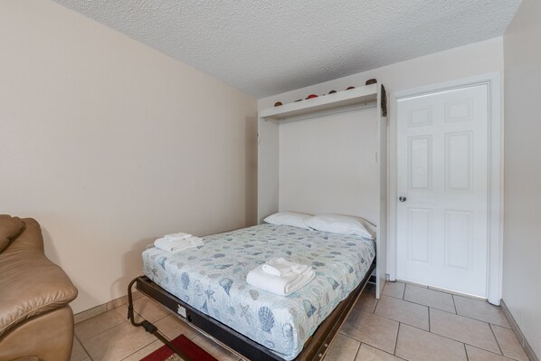 Un dormitorio con cama, una silla, una puerta y un estante con zapatos.