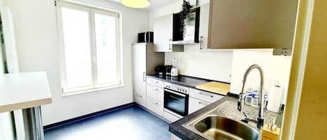Una cocina moderna con armarios blancos, horno integrado, lavamanos con grifo flexible y ventana que proporciona luz natural.