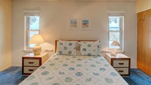 A bedroom with a bed, two nightstands, a ceiling fan, two windows with blinds, and two framed pictures on the wall.
