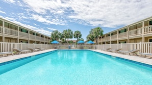 A swimming pool with lounge chairs and umbrellas, surrounded by a multi-story building with balconies.