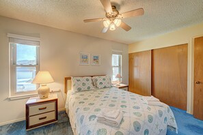 Un dormitorio con cama, mesitas de noche, ventilador de techo y ventana con persianas.